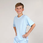 Young boy wearing a plastic free light blue sports t-shirt and shorts on a plain background