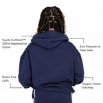 Back view of a girl wearing a Svante regenerative and organic cotton navy blue hoodie with text callouts highlighting product features: Svante Earthknit 100% Regenerative Cotton, Zero Polyester or Toxic Dyes, Plastic Free Cuffs, and Organic Cotton Stitching.