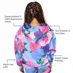 Back view of a girl wearing a light blue Svante organic cotton hoodie with a large pink and purple floral print, with text callouts highlighting fabric features like Svante Earthknit 100% Regenerative Cotton, Zero Polyester or Toxic Dyes, Organic Cotton Stitching, and Plastic Free Cuffs.