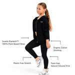 A girl modelilng a Svante polyester free black athletic leggings and matching organic cotton hoodie with text callouts highlighting fabric and stitching features on a white background.