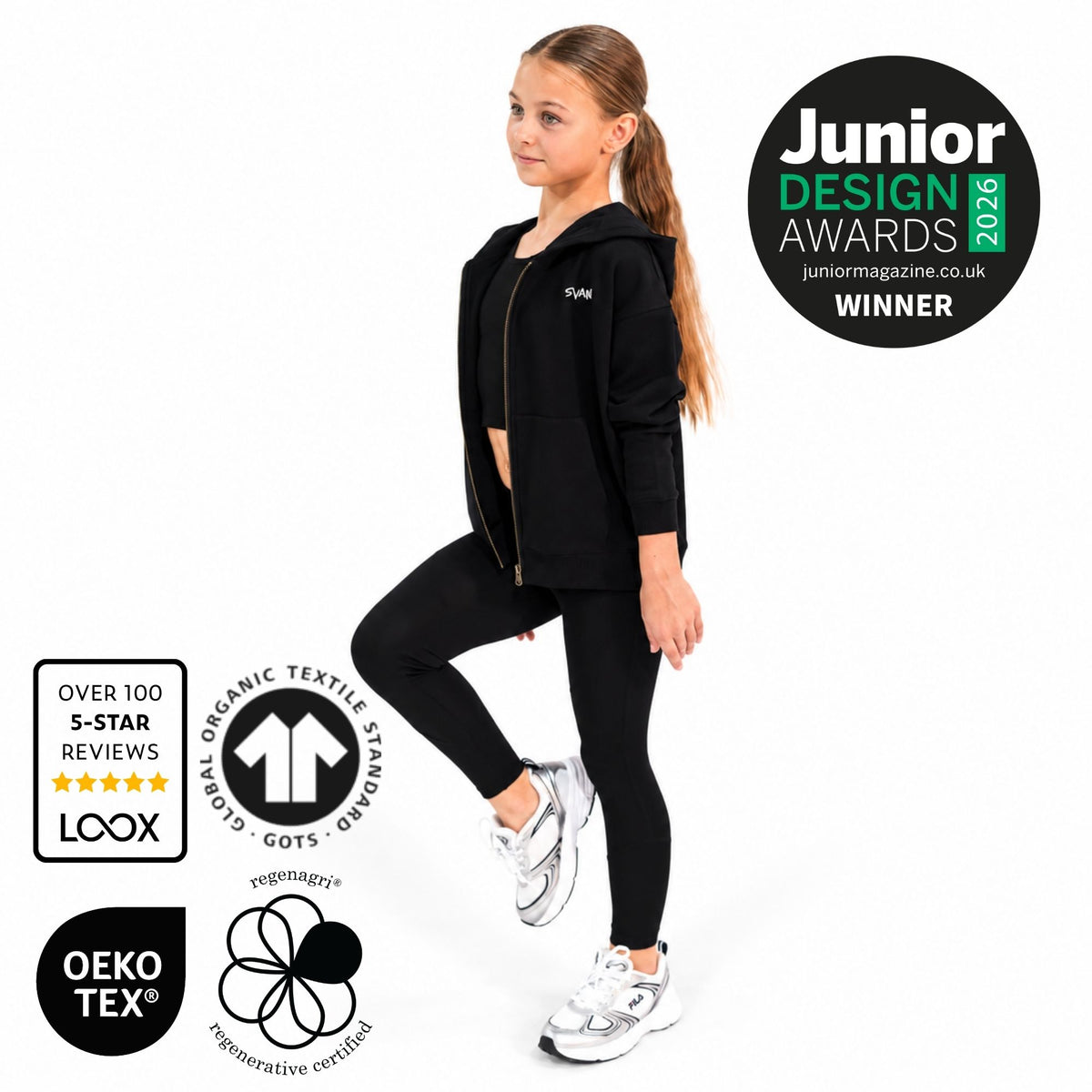 A young girl models a svante organic cotton black zip-up hoodie and matching black leggings set against a plain white background. The image includes several certification and award badges: a 'Junior Design Awards 2026 Winner' badge, a 'LOOX' organic textile review badge, and an 'OEKO-TEX' certification badge.