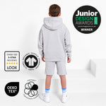 Boy with back to camera wearing a Svante grey organic cotton hoodie and grey organic cotton jersey shorts standing on a white platform. The image includes award and certification badges: a Junior Design Awards 2026 winner badge, LOOX over 100 5-star reviews badge, OEKO-TEX badge, and a Global Organic Textile Standard badge. 