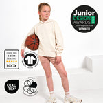 A young girl stands on white steps wearing a Svante regenerative cotton cream-coloured hoodie and polyester free sports shorts, holding a basketball. The image includes several certification and award badges, including 'Junior Design Awards 2026 Winner' from Junior Magazine and 'Over 100 5-Star Reviews' from LOOX.
