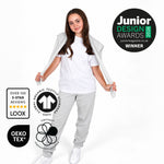 A young girl modelling a Svante regenerative cotton white t-shirt and Svante light grey sweatpants, with her white jacket draped off her shoulders, set against a plain white background. Multiple certification badges and award logos are displayed around her.