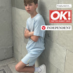 Boy in light blue microplastic free sports outfit leaning against a tiled wall with OK! and Independent logos.