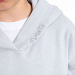Close-up of a person wearing a Svante Regenerative Cotton light grey hoodie with 'SVANTE' embroidered vertically on the hood, layered over a white t-shirt.