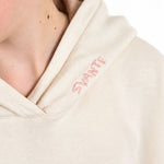 Close-up of a girl wearing a Svante organic cotton cream-coloured hoodie with a pink embroidered 'SVANTE' logo on the shoulder.