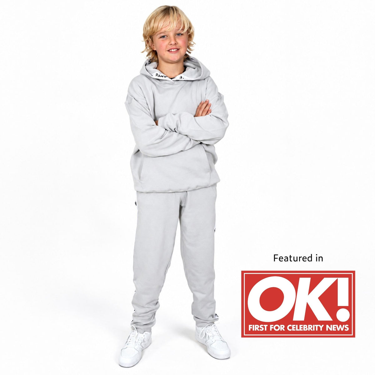 Boy wearing a Svante regenerative cotton hooded sweatshirt and matching jogger pants with white sneakers. A red 'Featured in OK! FIRST FOR CELEBRITY NEWS' badge appears in the lower right corner. 