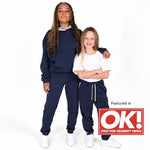 Two girls modelling matching Svante organic cotton navy blue sweatshirt and jogger pants sets against a white studio background. The older girl wears a Svante navy hoodie and joggers, while the younger girl wears a white t-shirt and navy joggers. 
