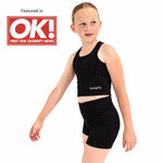 A young girl modelling a Svante black dance set consisting of a sports crop top and matching shorts, with the brand name 'SVANTE' printed in white on the front of the top. She is posed against a solid white background, with a 'Featured in OK! FIRST FOR CELEBRITY NEWS' badge in the upper left corner.