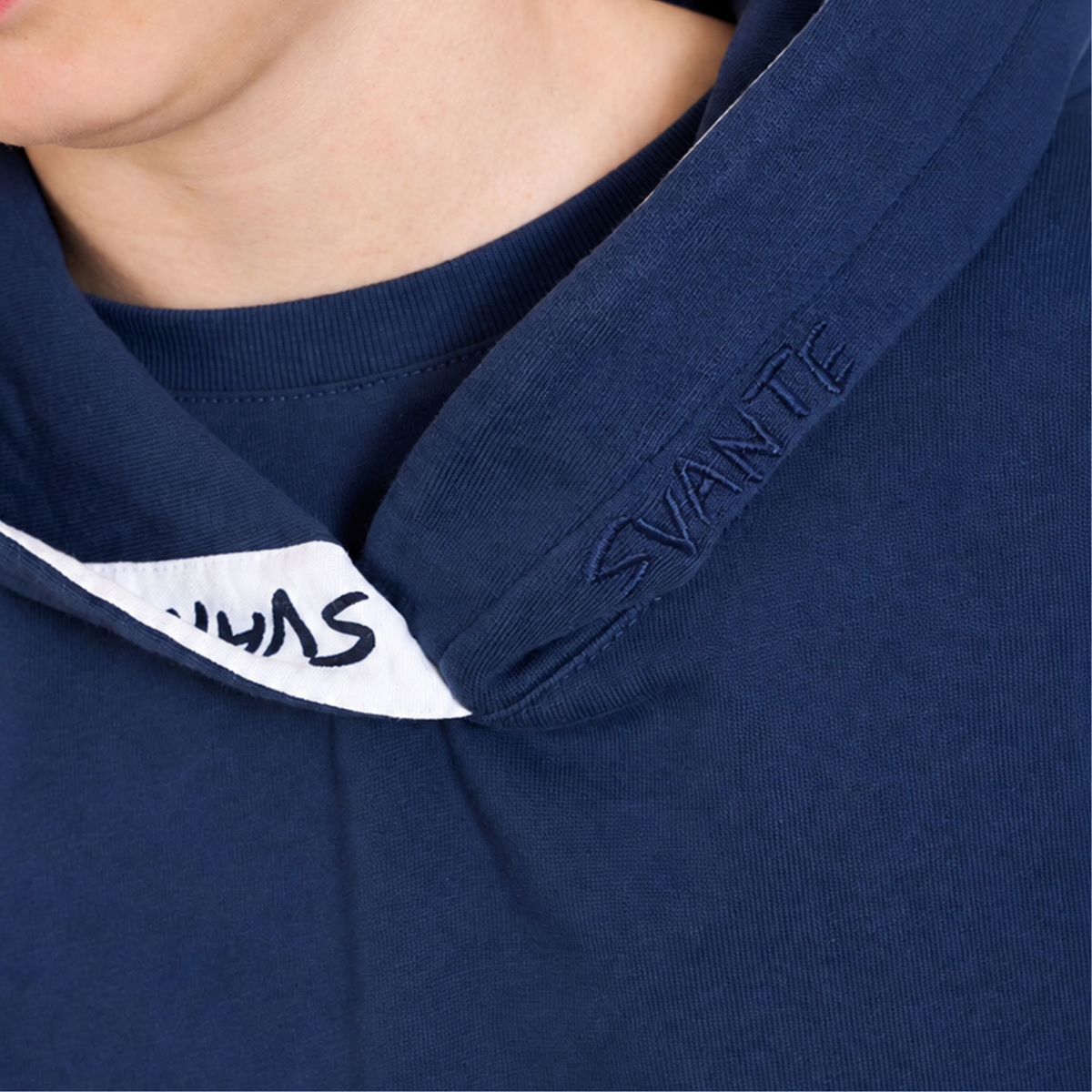 Close-up of a Svante regenerative and organic cotton navy blue hooded sweatshirt with a white inner hood lining and the brand name 'SVANTE' embroidered on the hood.