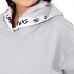 Close-up of a person wearing a Svante regenerative cotton light grey hoodie with a white inner hood lining printed with black stylized lettering and logos.