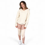 A teenage girl modelling a Svante regenerative cotton cream-coloured hooded sweatshirt and colour-blocked, polyester free sports leggings in beige and dusty rose, paired with white sneakers, against a solid white background.