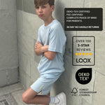 Boy wearing all natural plastic free light blue sports t-shirt and shorts against a tiled wall with LOOX branding and certification logos.