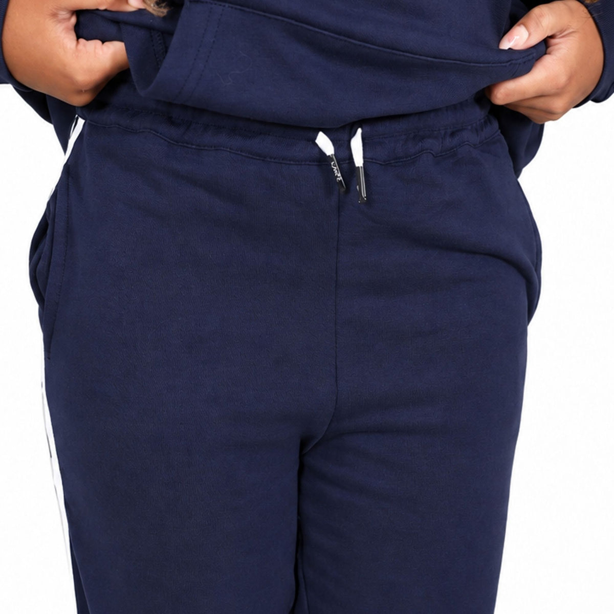 Close-up of a girl wearing a Svante navy blue sweatpants, pulling the matching sweatshirt hem down slightly to show the elastic waistband and drawstrings. 