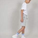Boy wearing a white organic cotton t-shirt, organic cotton grey jersey shorts, and white socks with blue stripes on a plain background. 