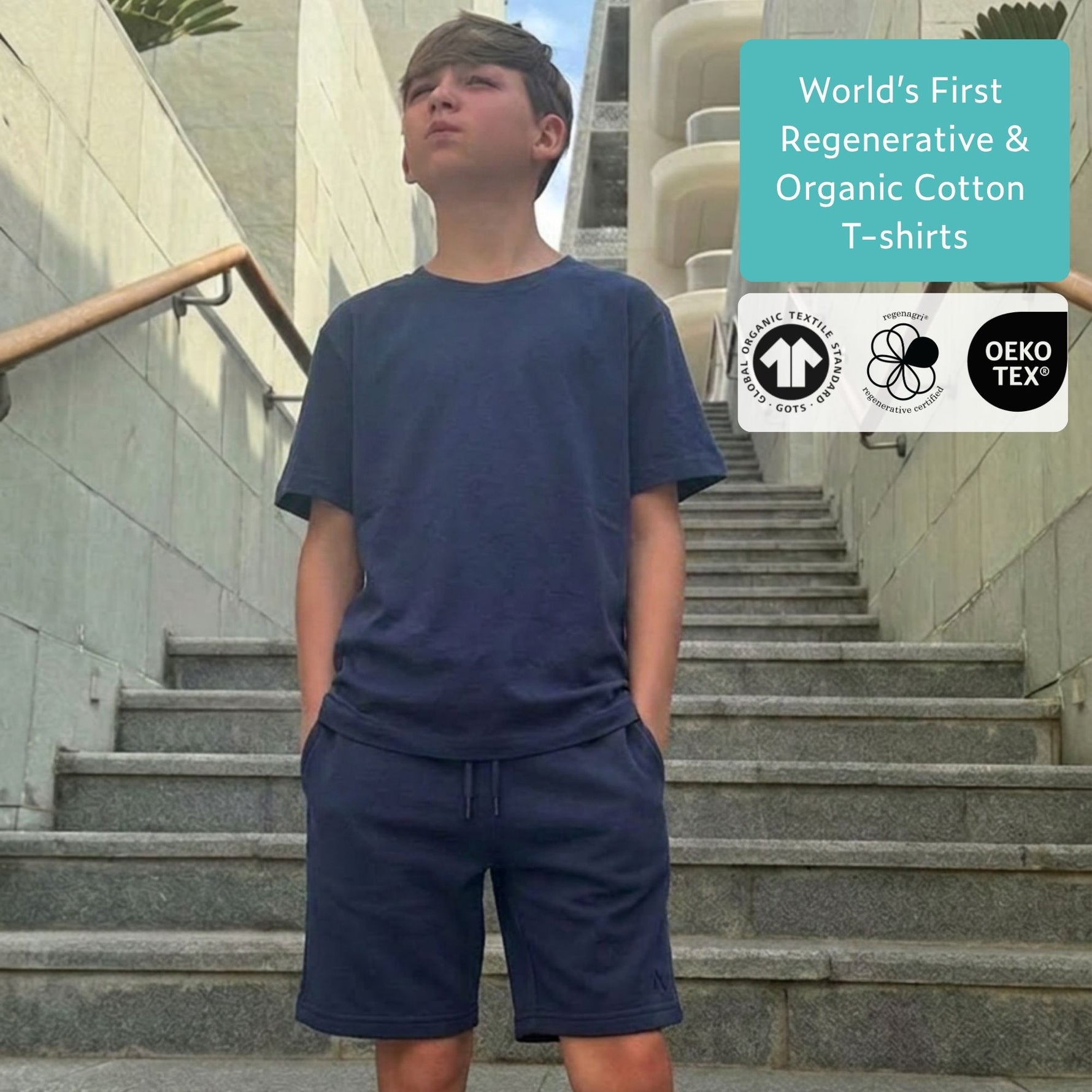 Boy wearing a navy blue regenerative cotton t-shirt and blue organic cotton jersey shorts set on stone steps with text about regenerative and organic cotton t-shirts. 