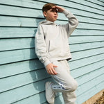 Boy leaning on teal green wall wearing Svante grey organic cotton hoodie with grey regenerative cotton joggers. 