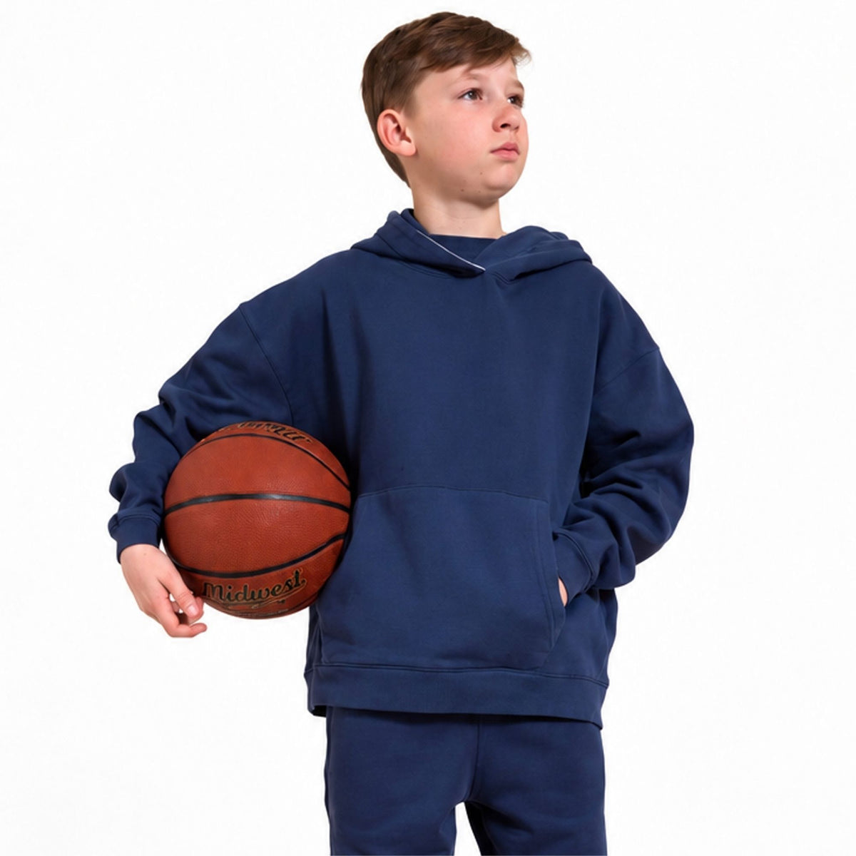 Boy wearing an organic cotton navy blue hoodie and matching sweatpants, holding a brown basketball against a plain white background. 