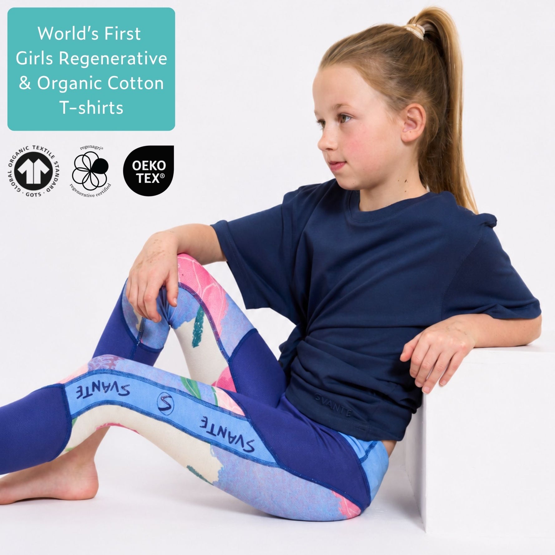 Girl wearing a blue organic cotton T shirt and blue sports leggings with 'Svante' branding, sitting on a white surface. #Peacoat-Blue
