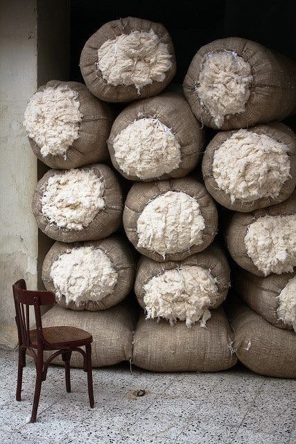 Stack of burlap sacks filled with organic cotton next to a wooden chair.