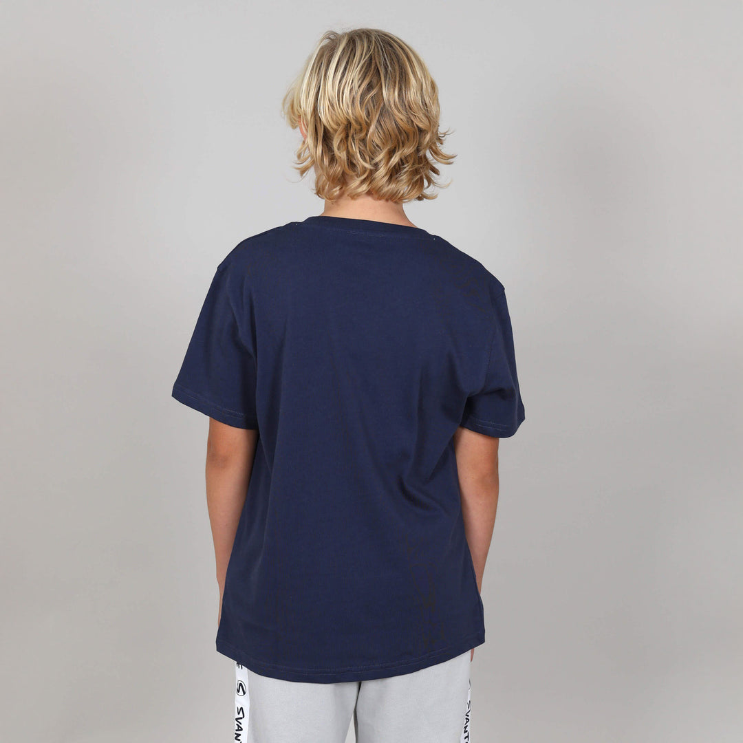 Boy with back to camera showing backside of an organic navy blue t-shirt on a plain background. 