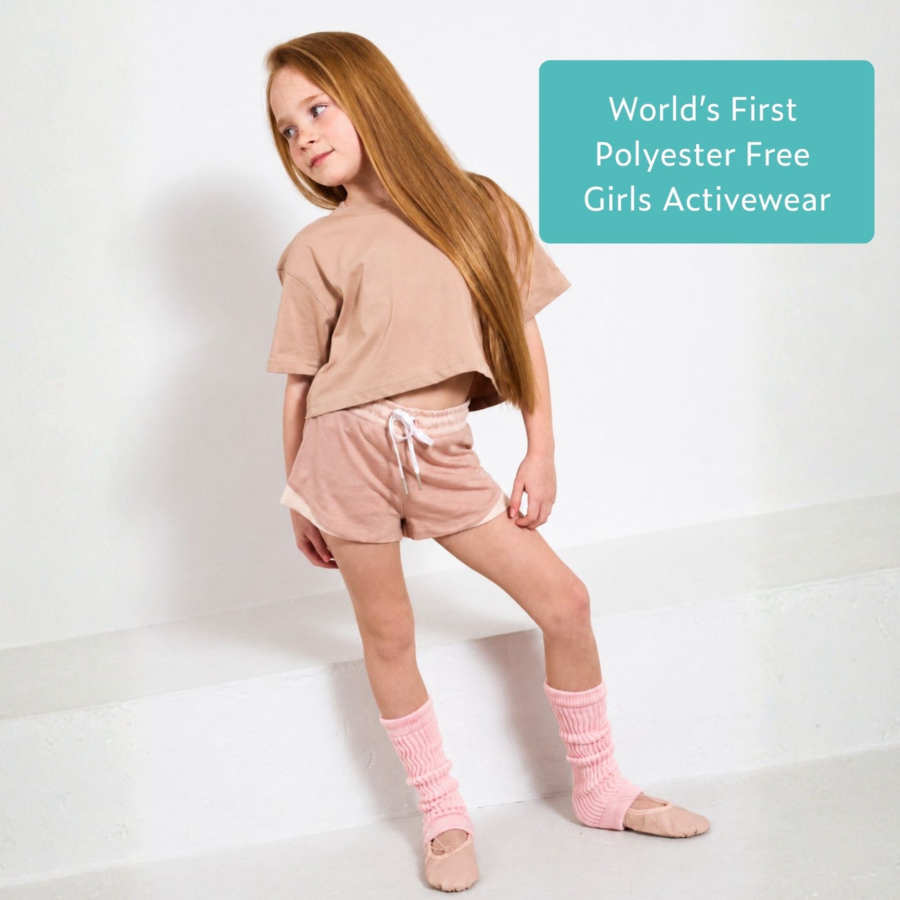 Young girl wearing pink organic cotton crop top and pink sports shorts with text 'World's First Polyester Free Girls Activewear' on a white background. 