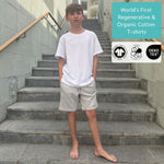 Boy wearing an organic cotton white t-shirt and grey regenerative cotton jersey shorts standing on stairs with Oeko-Tex and OEKO-TEX logos displayed. 