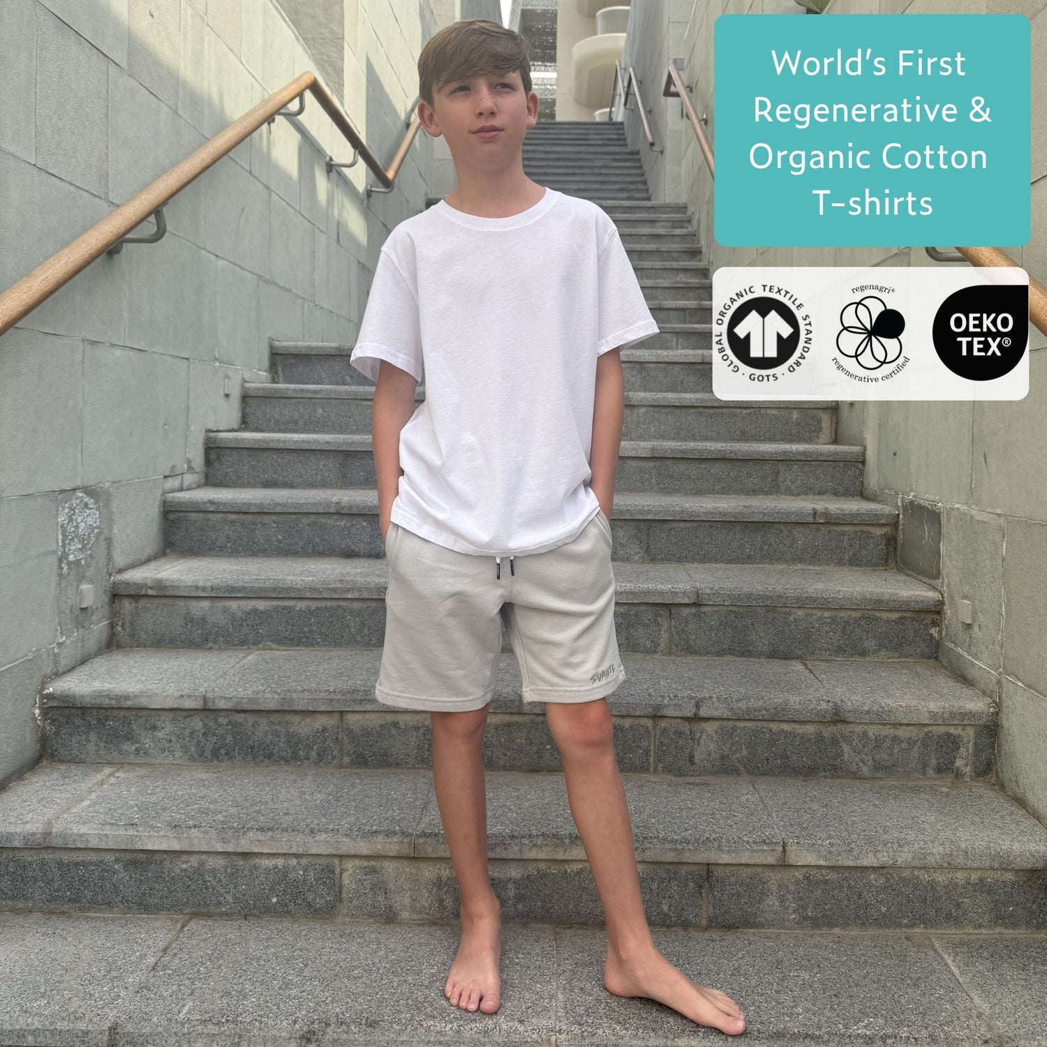 Boy wearing an organic cotton white t-shirt and grey regenerative cotton jersey shorts standing on stairs with Oeko-Tex and OEKO-TEX logos displayed. 