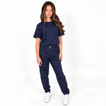 A young girl modelling a Svante regenerative and organic cotton matching navy blue lounge set, consisting of a short-sleeve crewneck t-shirt and jogger-style pants with a drawstring waist, paired with white sneakers, against a plain white studio background.