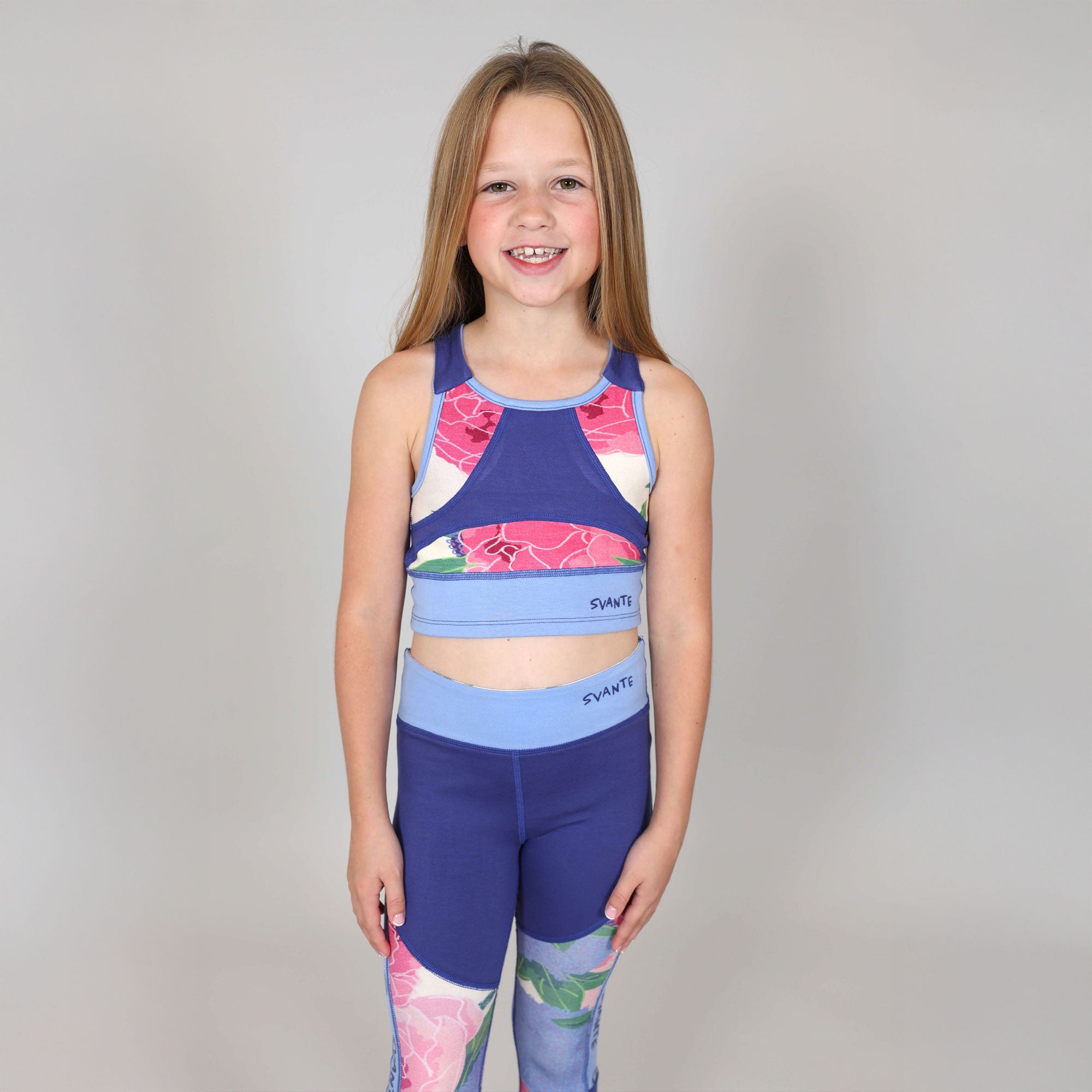 Young girl with big smile facing camera wearing a colourful floral sports bra and leggings set on a plain background
